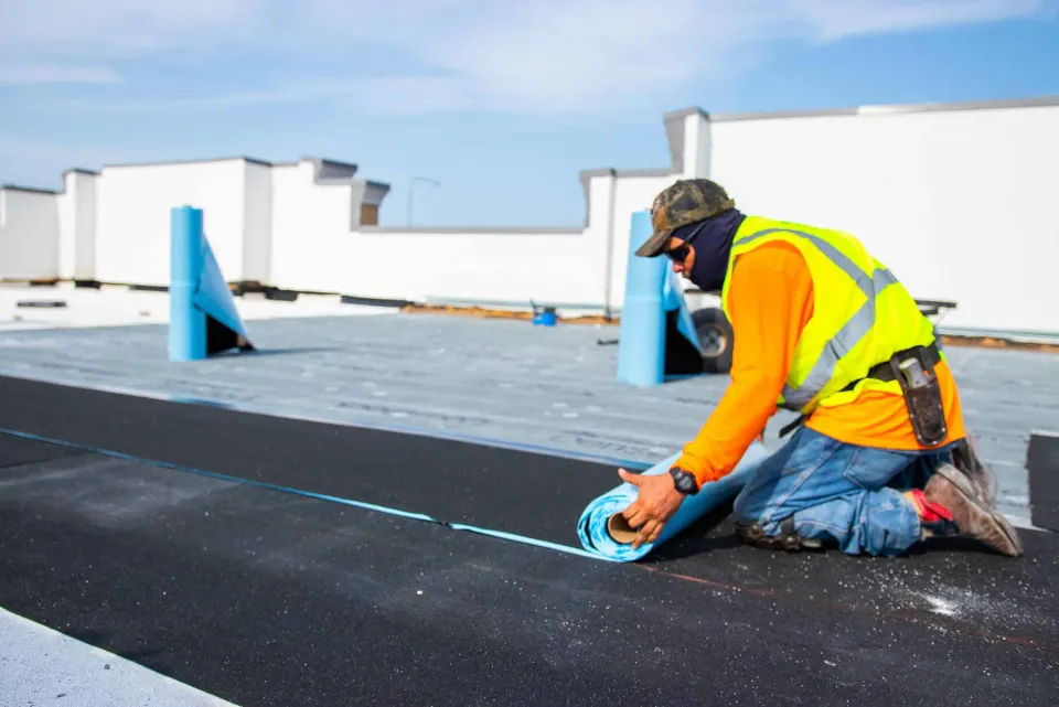 Worker unrolling self-adhering membrane on a commercial low-slope roof